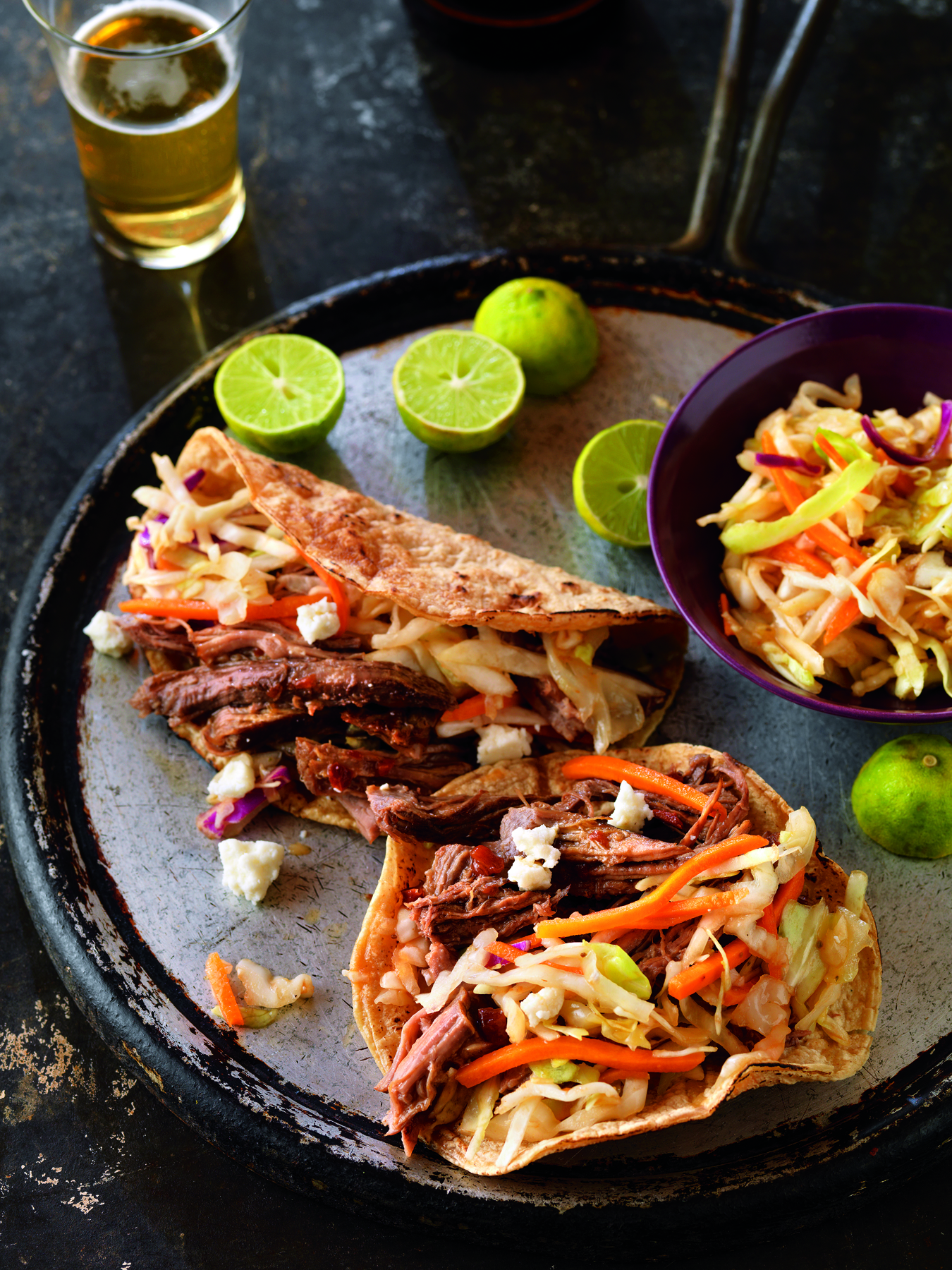 Bear River Valley Beef - Beef Cuts Delicious pulled beef tacos topped with fresh coleslaw, served on a rustic plate with lime wedges and a glass of beer, perfect for a casual dining experience.