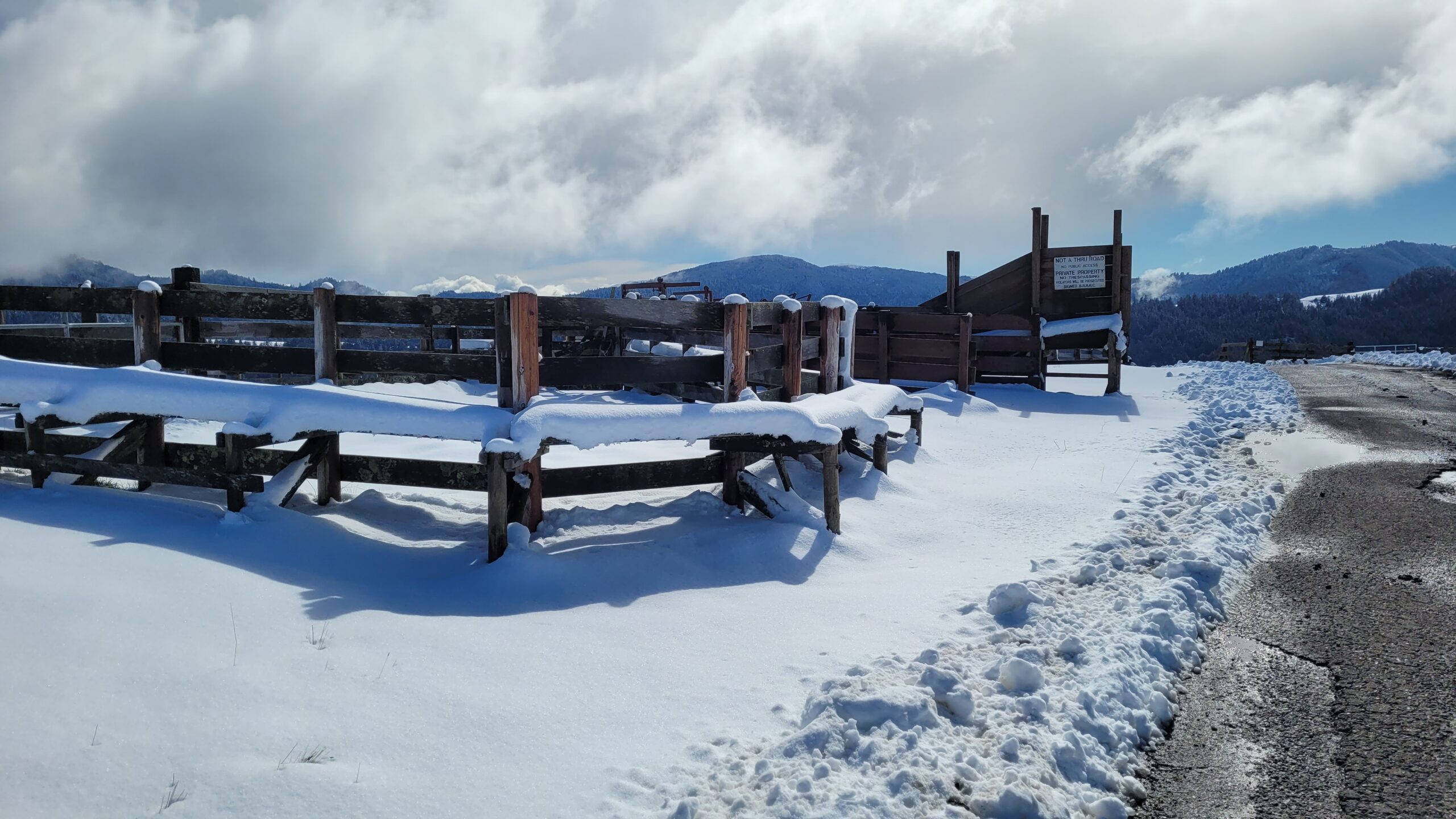 Liz Klopper - snow corrals Snow-covered wooden fence and entry gate in a mountainous area, with a clear blue sky and clouds in the background. The scene captures the tranquility of winter landscapes, ideal for outdoor enthusiasts and nature lovers.